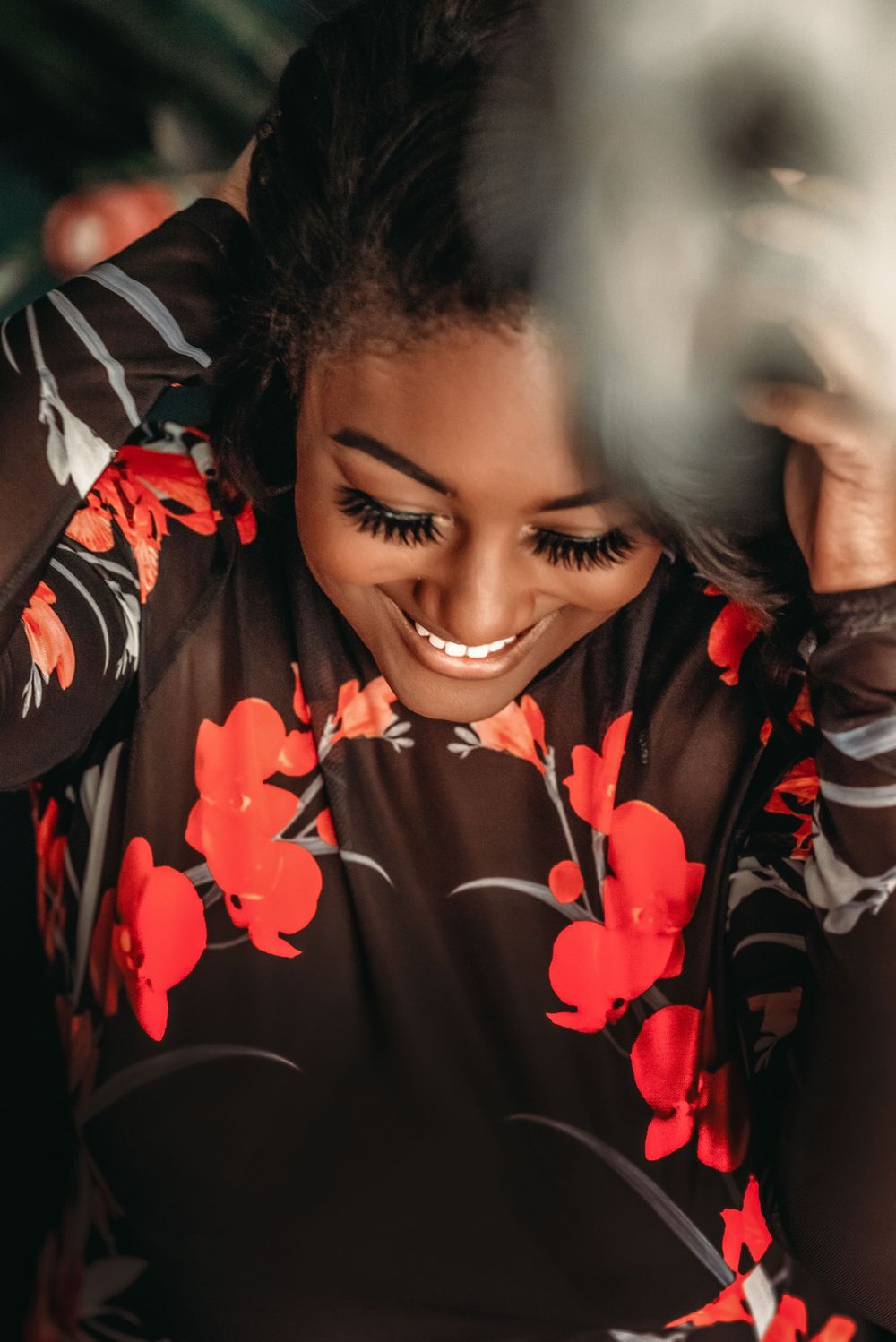 boudoir photo of a woman wearing a sheer black and floral bodysuit looking down holding her long hair and smiling
