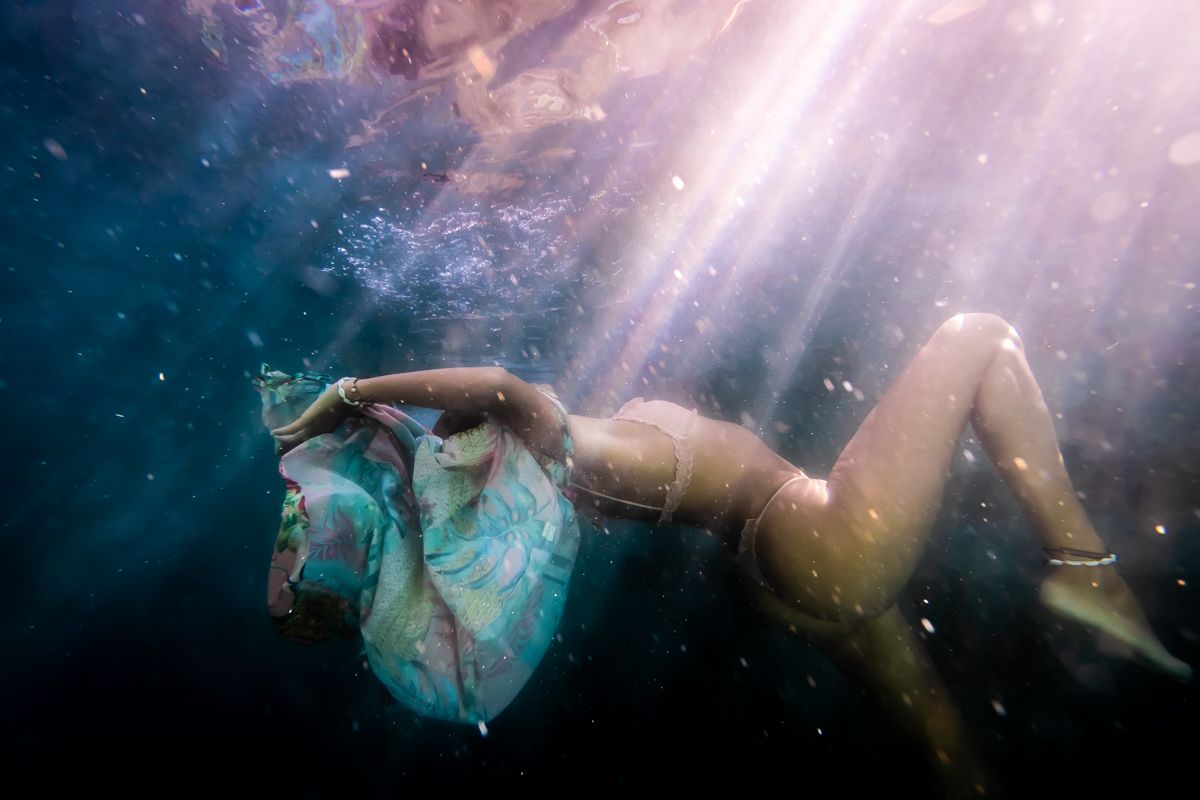 A woman falling through water with sun beams on her body