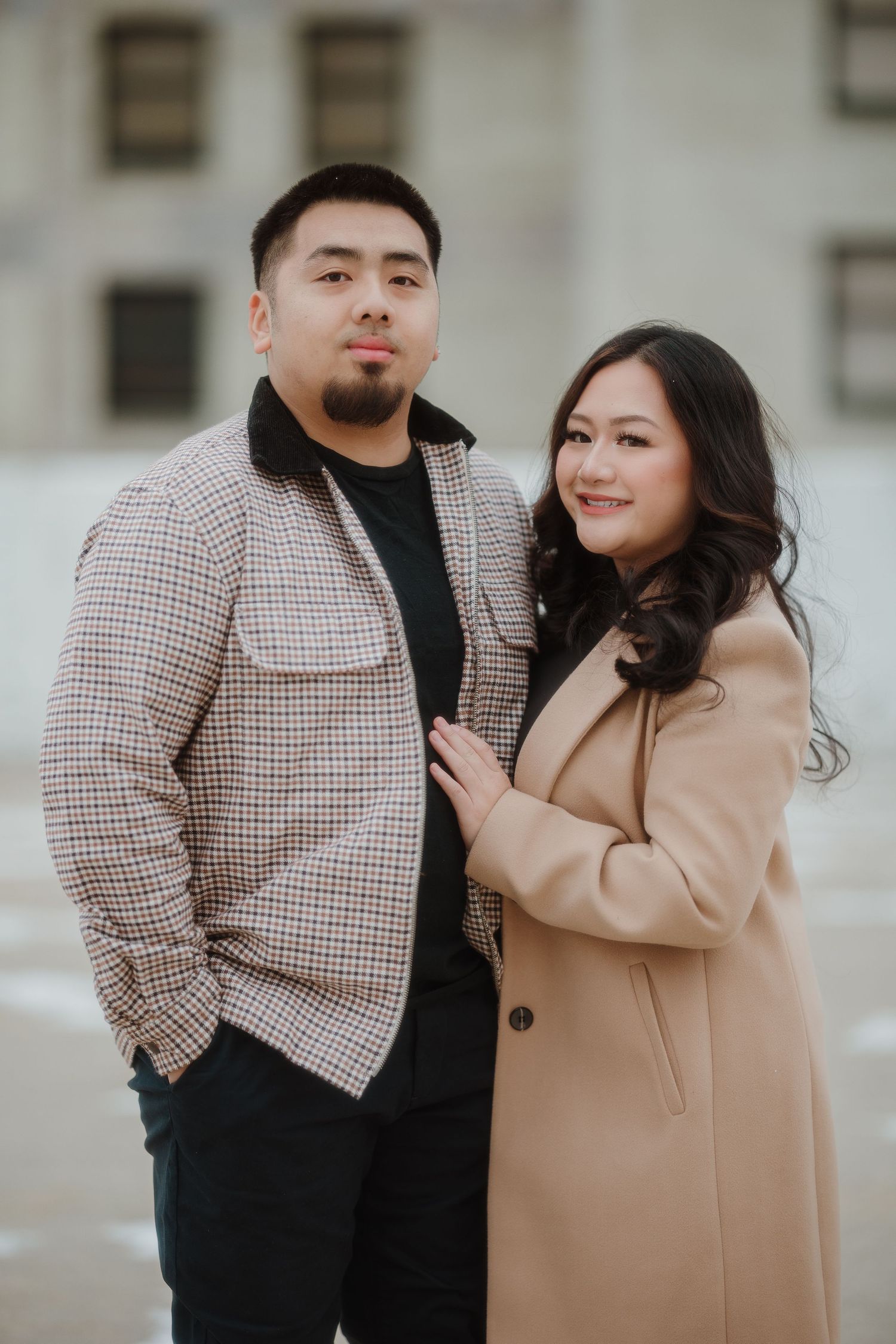 A couple poses together in coordinated outerwear for a portrait against an urban backdrop.