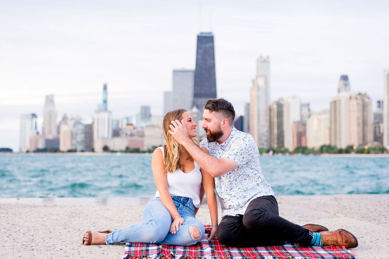 dark hair man pushes back hair of his blonde fiance while they sit at North Avenue Beach