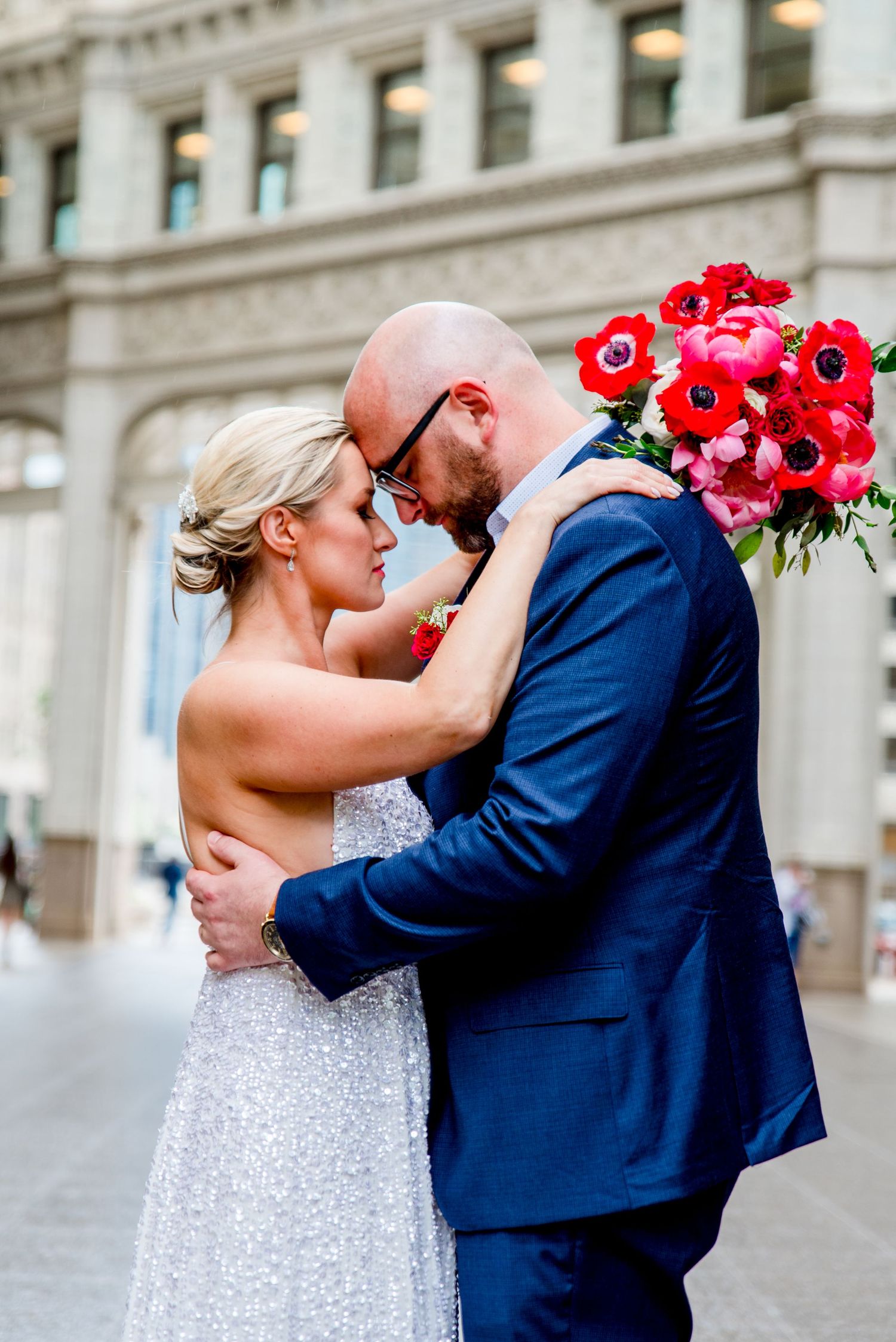 couple in navy suit and glittery dress with red bouquet walking under Wrigley building at Chicago Elopement