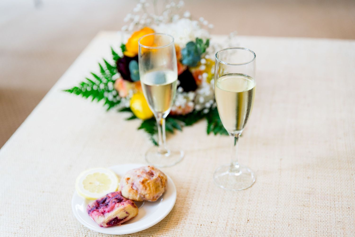 two glasses of champagne and a plate of breakfast pastries with wedding bouquet on a table