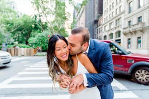 man in navy suit hugging and kissing fiance in white dress at corner of streets in NYC