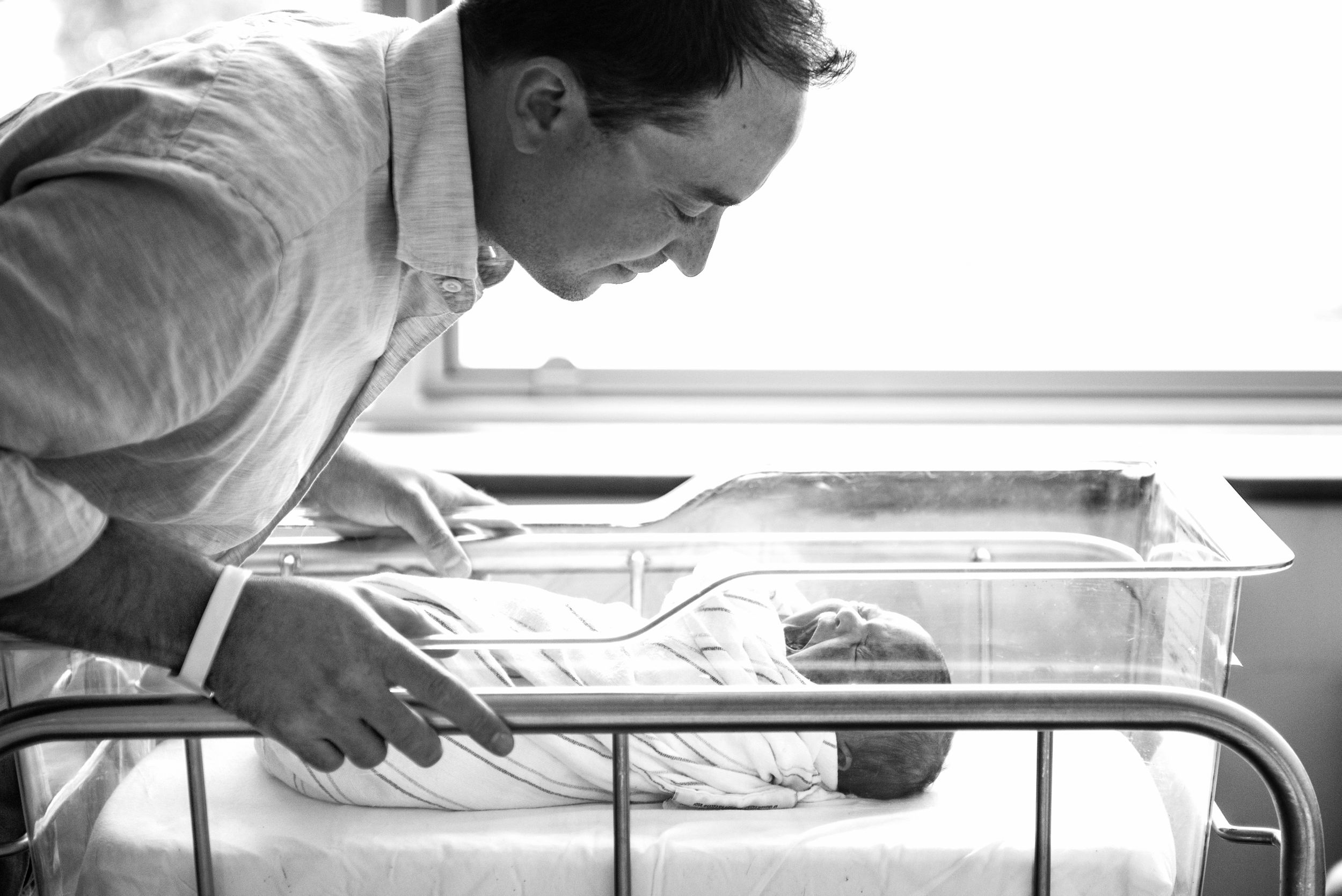 New father leaning over bassinet gazing at newborn captured in a Fresh 48 Session by Heidi Harting Photography