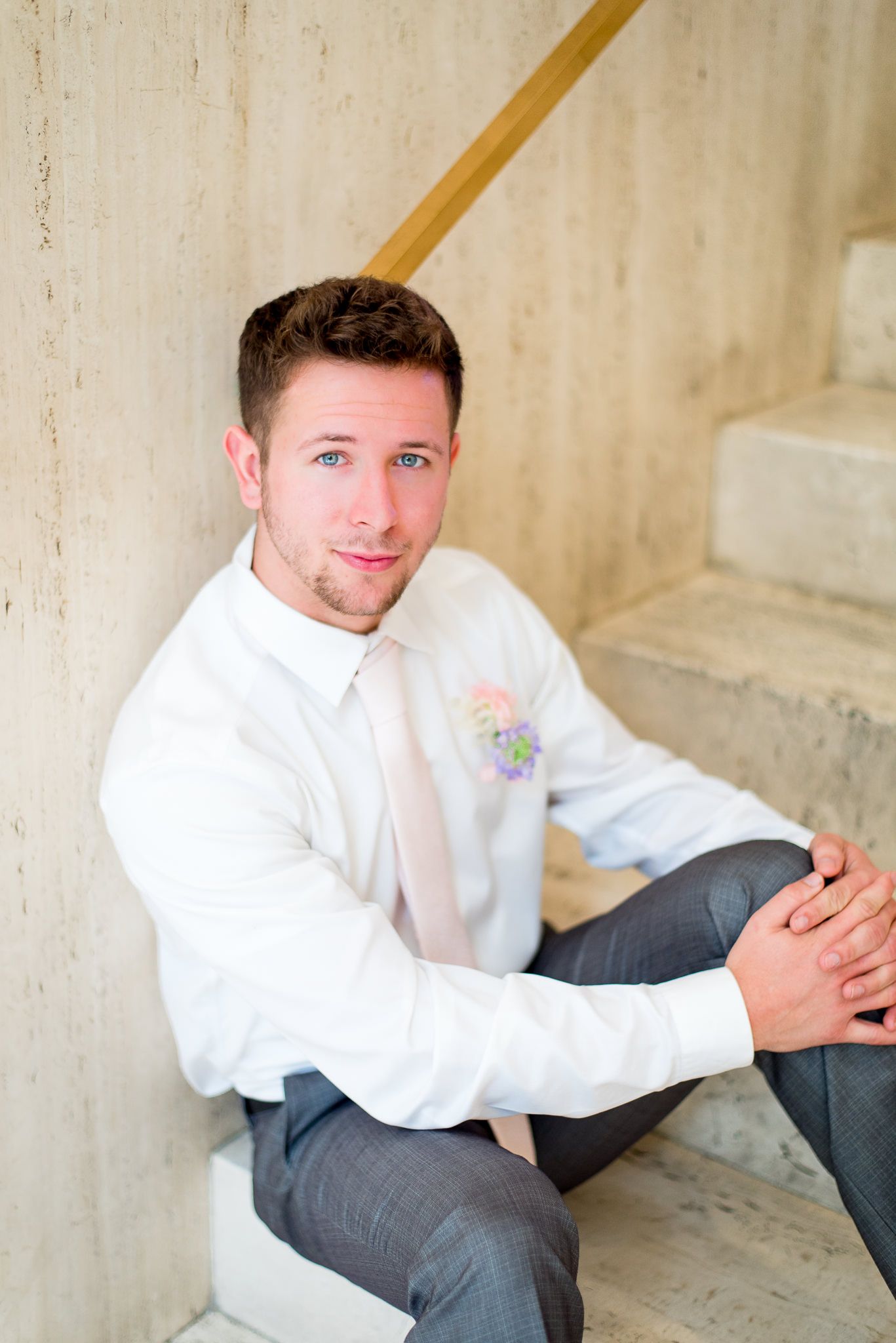 groom with blue eyes, light pink tie, and pink and purple boutonniere sitting on marble steps at The Center Cincinnati