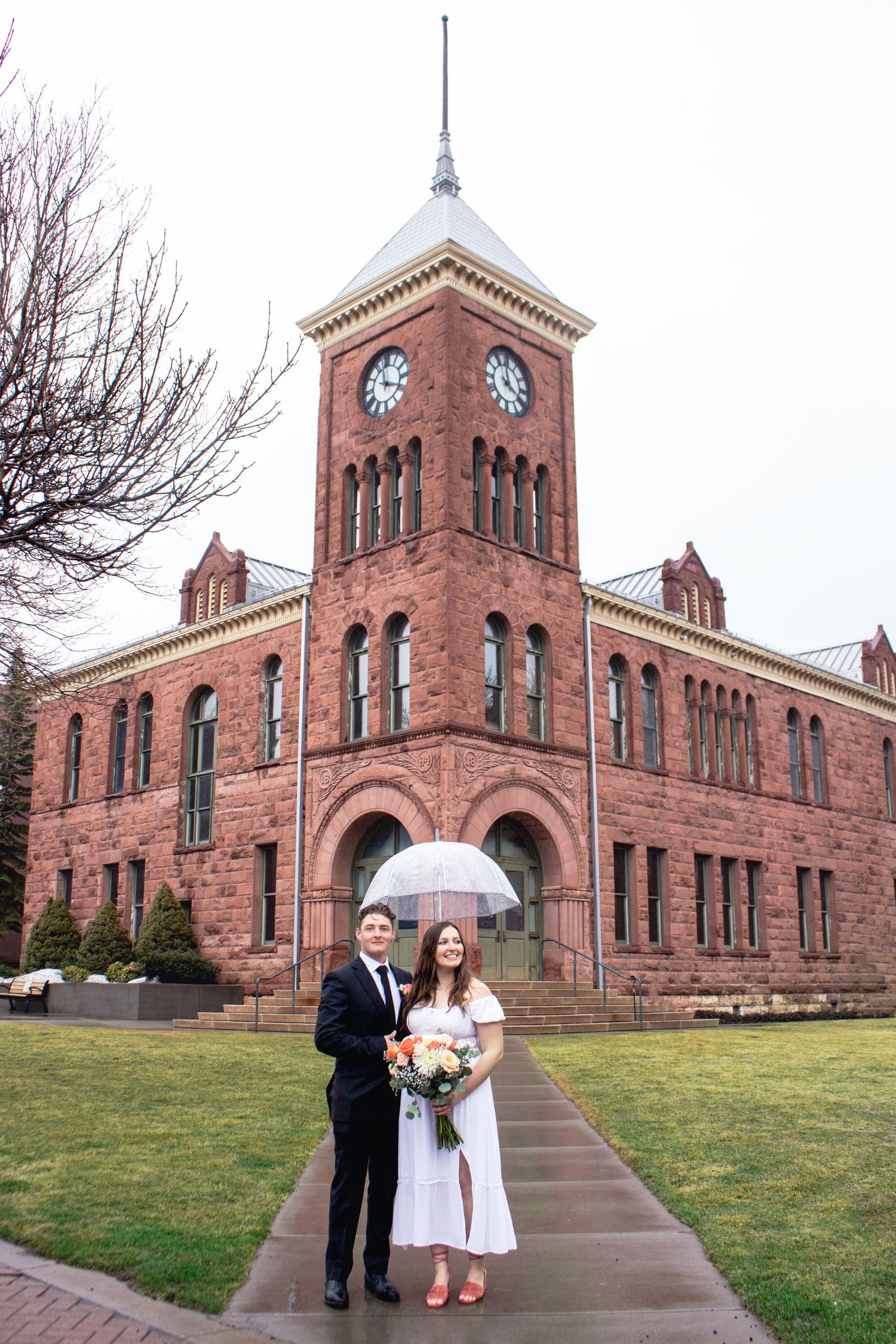Wedding couple poses in front of historic red brick clock tower building.