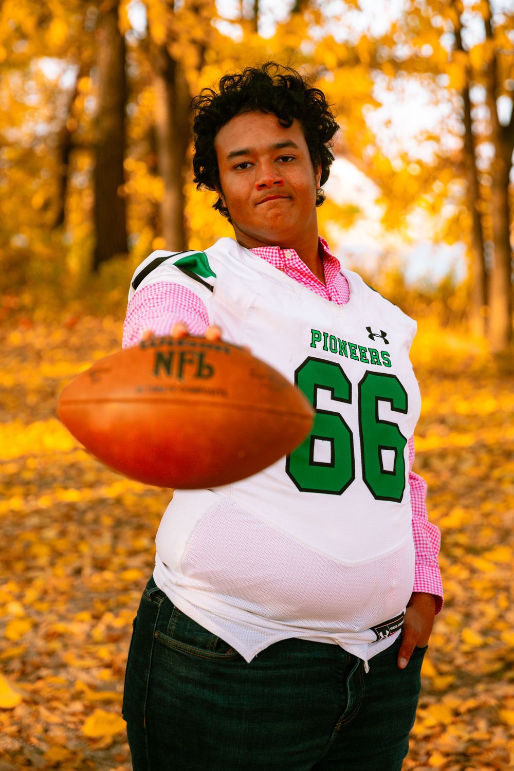 senior football player in uniform in front of fall colors