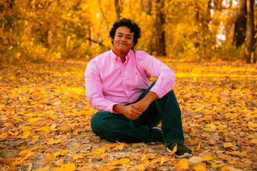 senior boy sitting on a leafy path with leaves falling around him