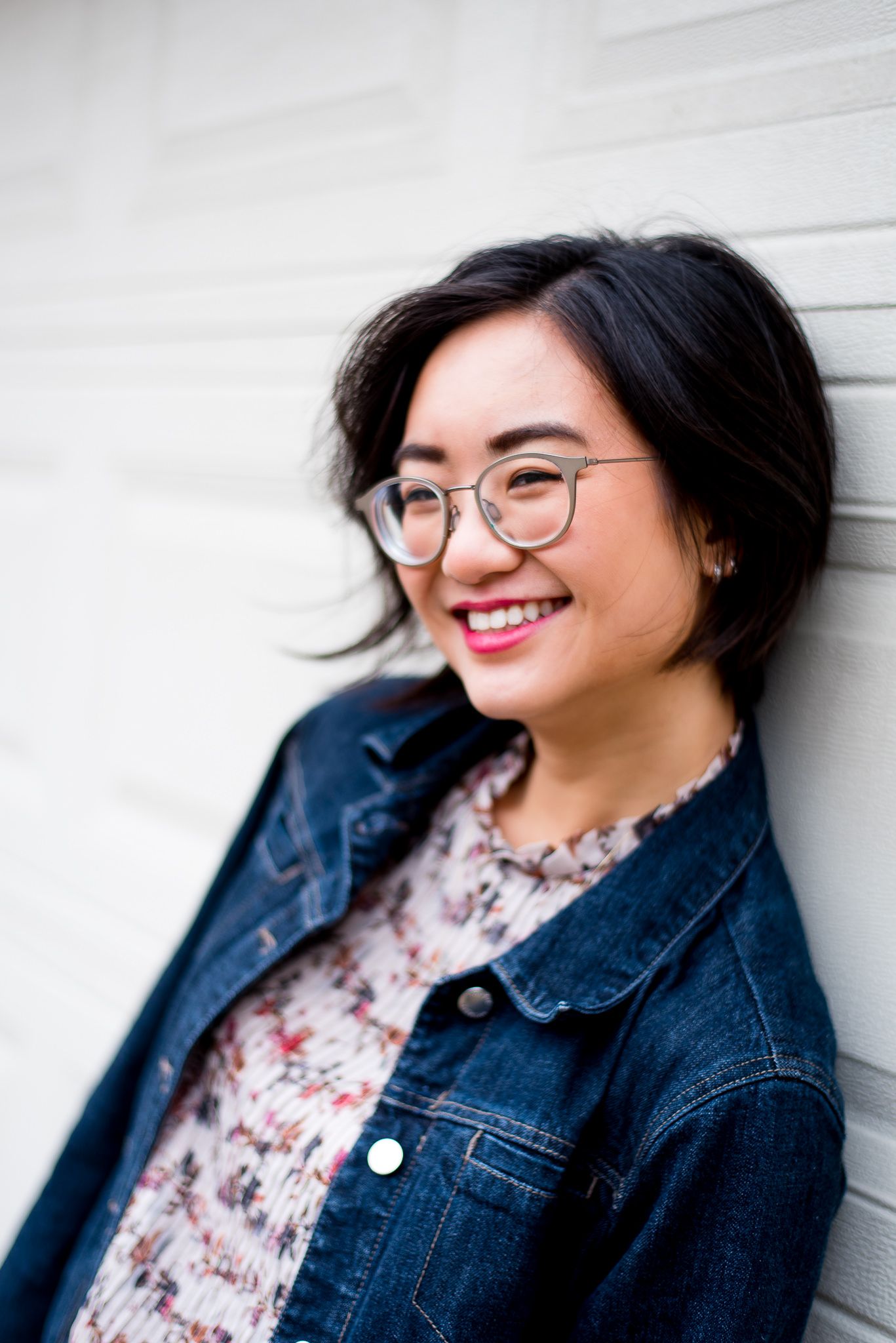 young asian woman with chin length hair leaning against a white garage door for chicago senior pictures
