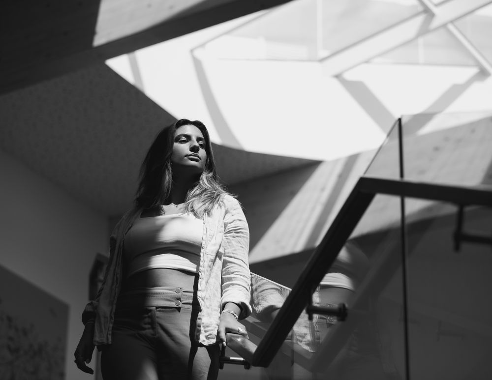 Black and white image of a young woman pausing whilst walking down a large staircase