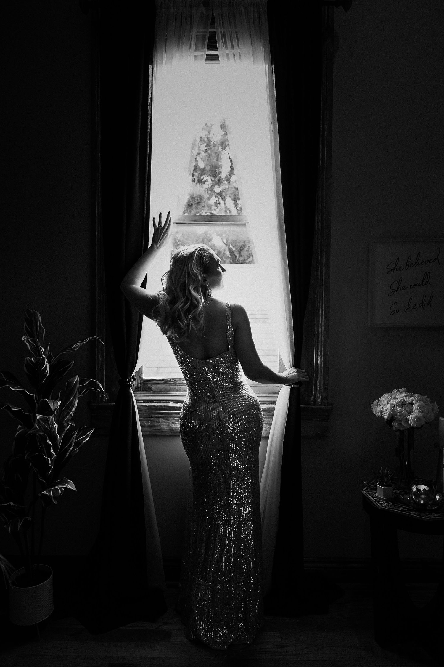 Silhouette of a person in a sparkly gown standing by a bright window.