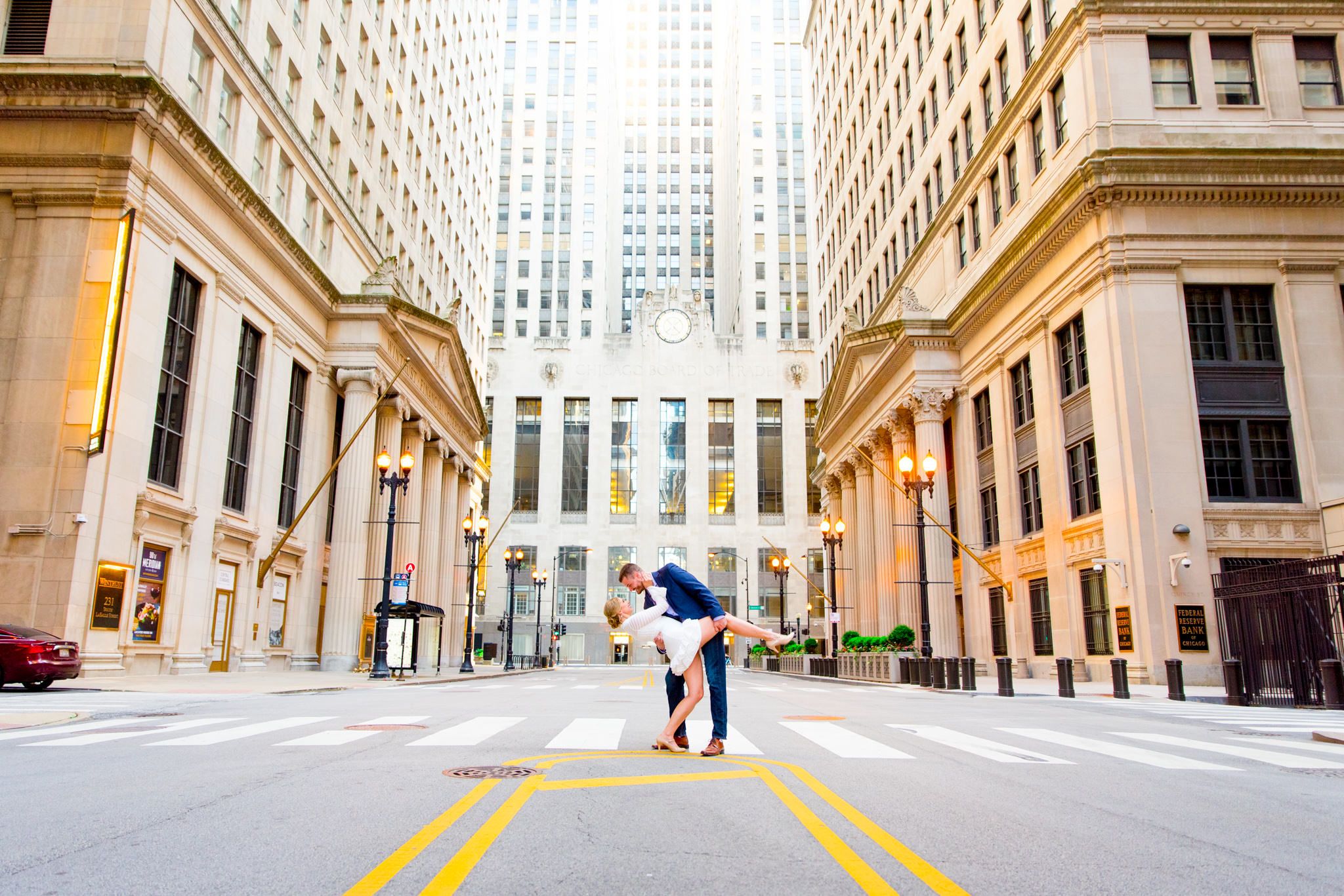 man in navy suit dipping woman in white dress in front of Chicago Board of Trade for engagement pictures