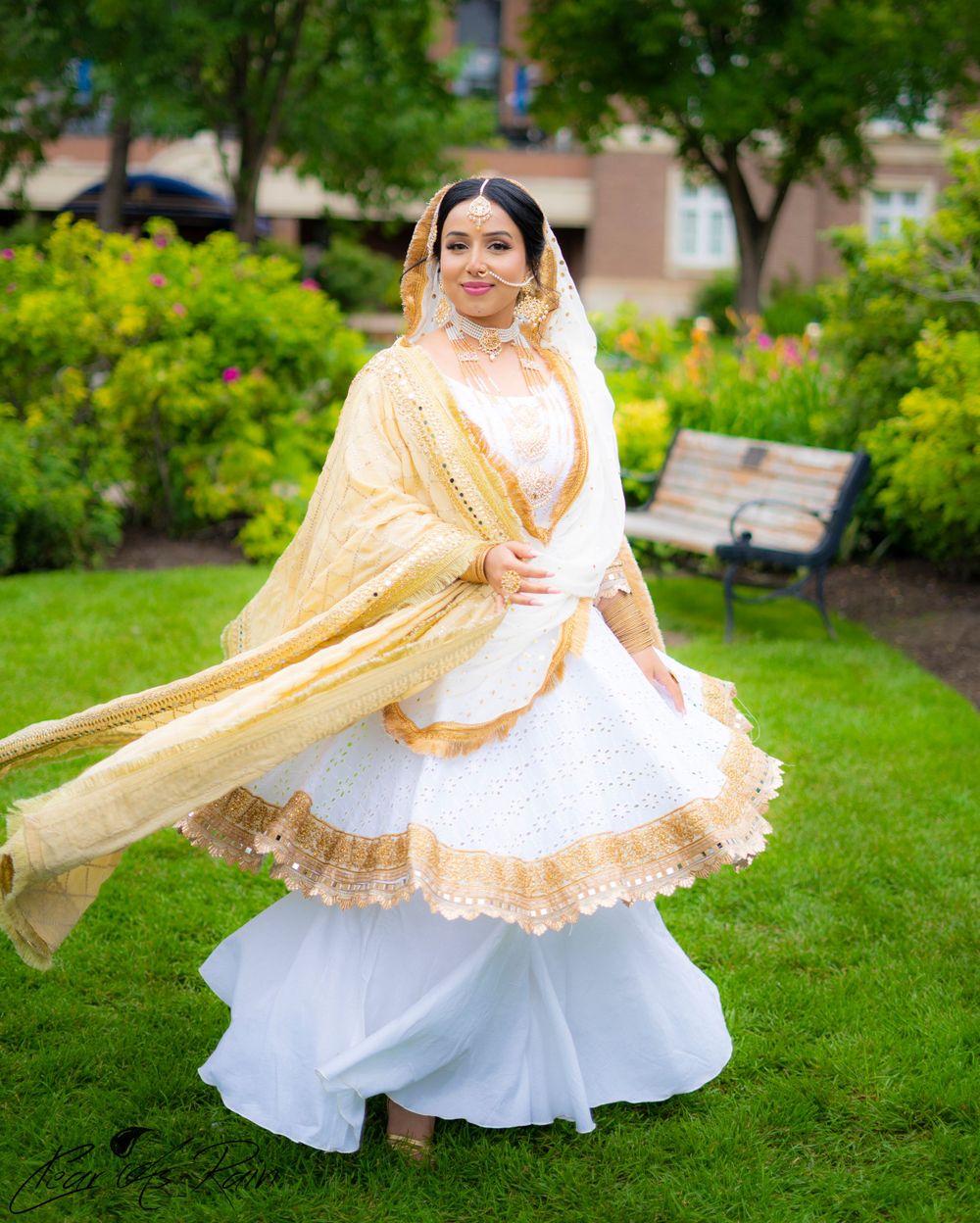 Traditional South Asian bride in white and gold lehenga twirls gracefully in a garden setting.