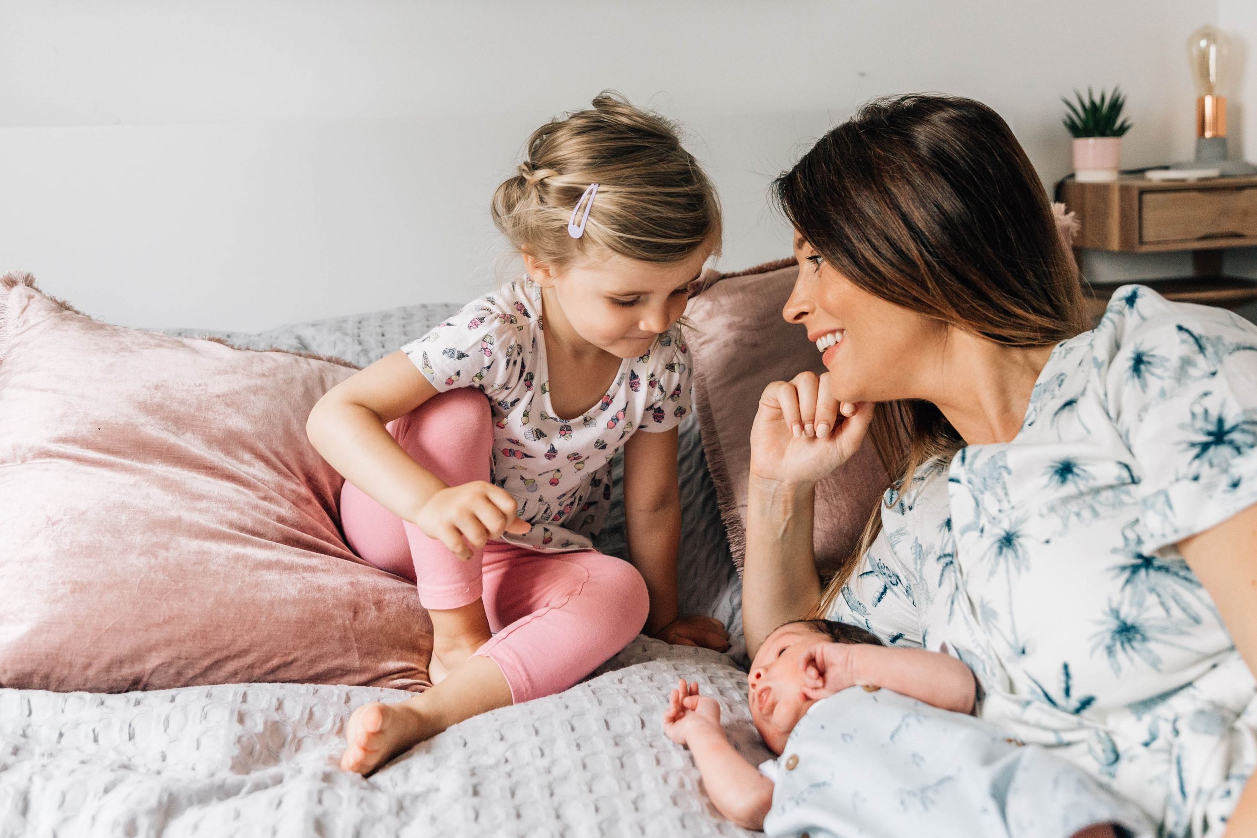 mum toddler girl and newborn baby boy on bed smiling