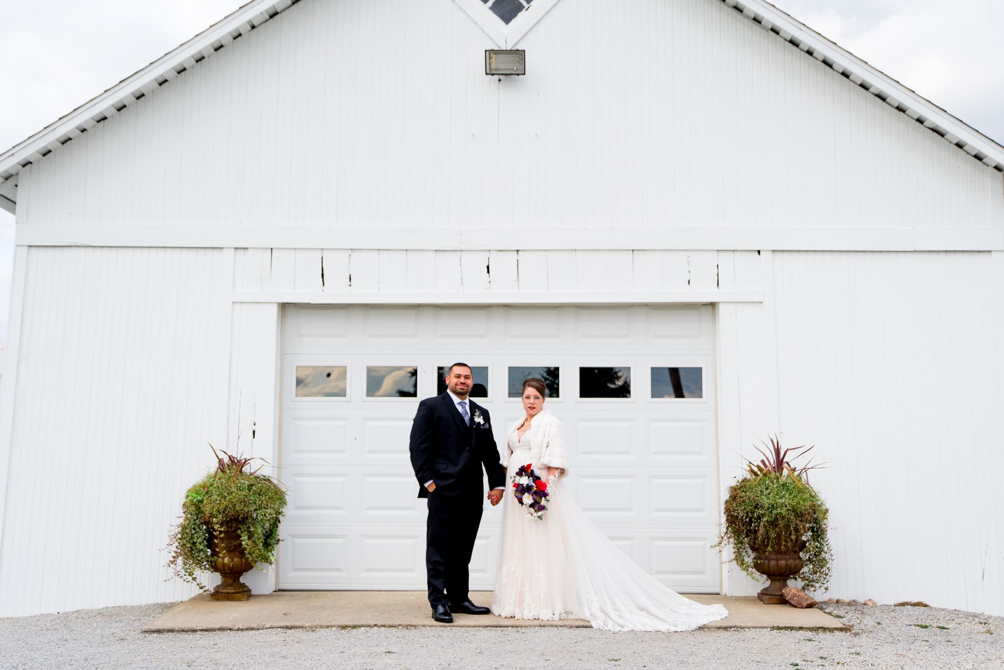 bride and groom holding hands in front of white barn with white garage door