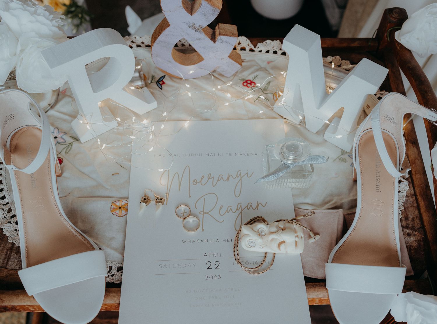 Wedding details flatlay with white heels, invitation and decorative lettering with fairy lights.
