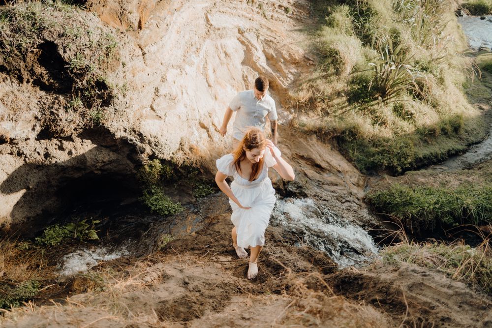 A couple dances joyfully near a rocky cliff with ocean views.