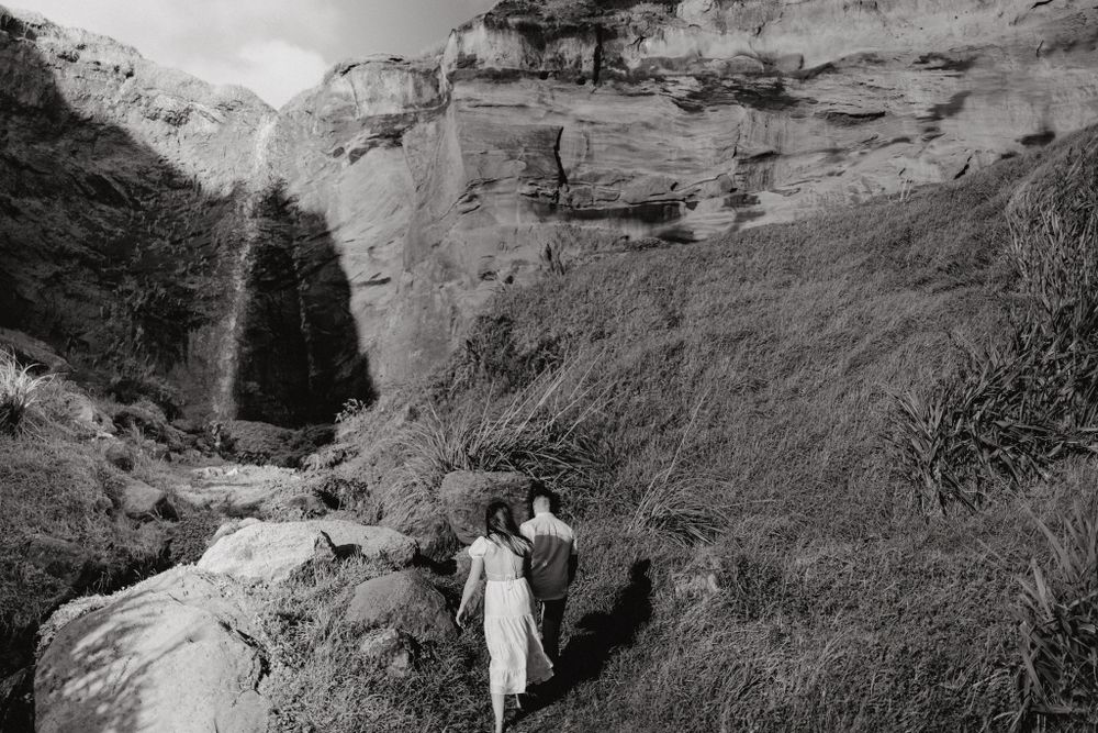 A black and white portrait of a couple near a dramatic waterfall cliff face.
