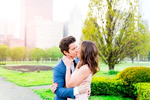 man in navy suit and woman in pink dress kiss in the middle of Millennium Park in front of Chicago skyline