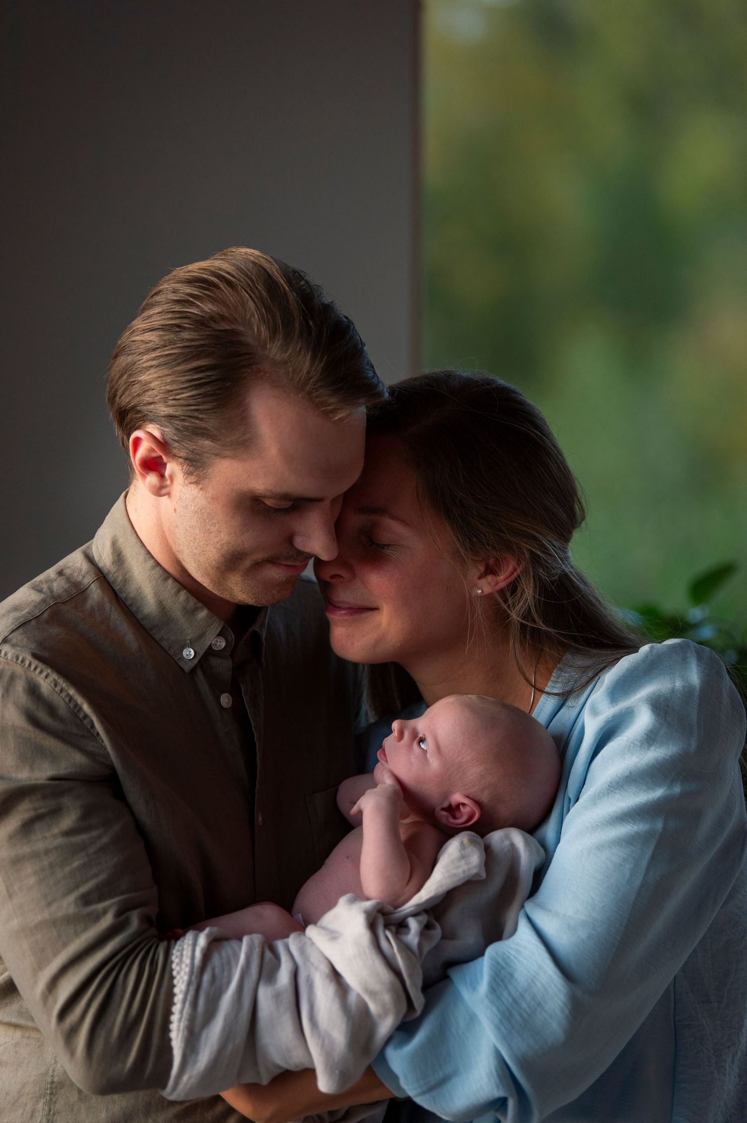 mamma och pappa håller tillsammans deras son, mamman lutar sig in mot pappans axel och ler.