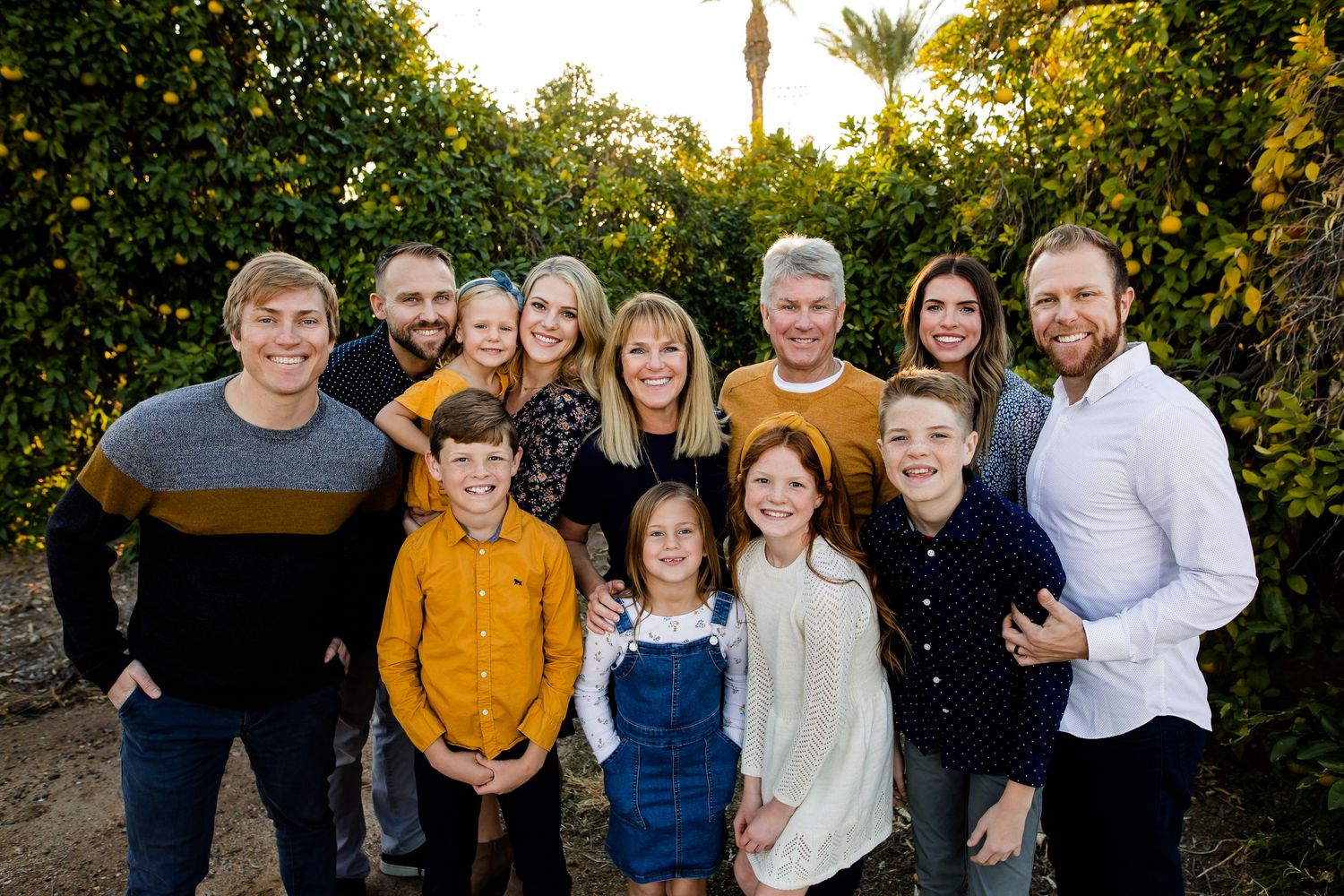 A large extended family huddled together and smiling for a fun group portrait in the farm orchards of Arizona at sunset.