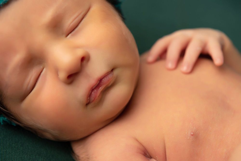 Sleeping newborn wrapped in brown textured blanket against dark brown background.