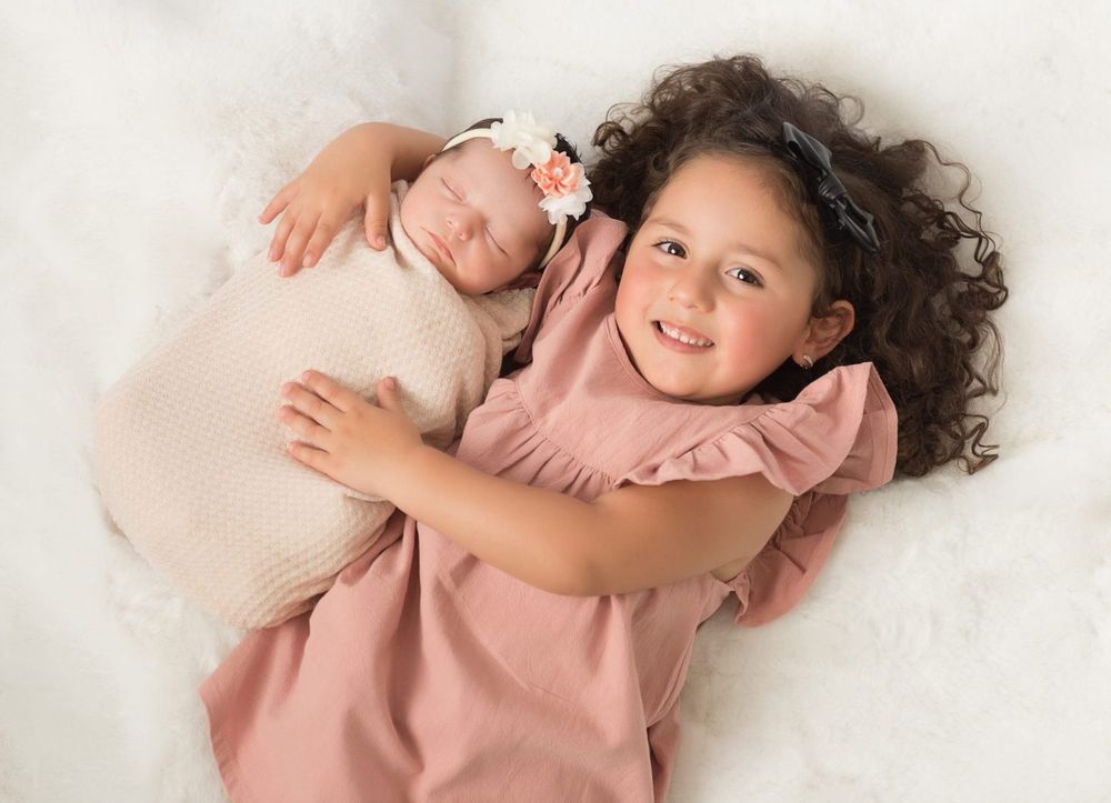 Sweet sibling moment on white background with young child and sleeping baby.