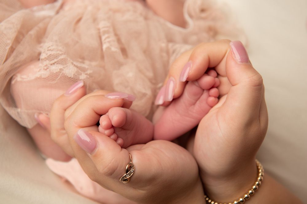 Tiny newborn feet being gently cradled in adult hands with jewelry.
