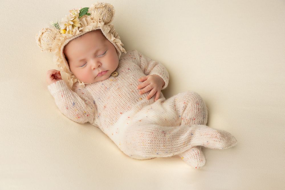 Peaceful newborn in cream knit outfit wearing floral crown.
