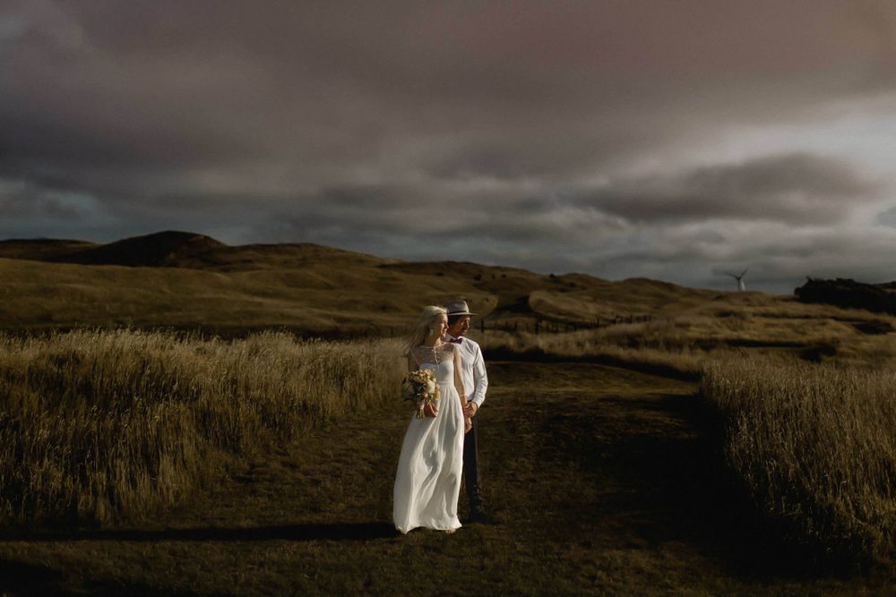 A figure in white stands on a moody hillside path under dramatic stormy skies.