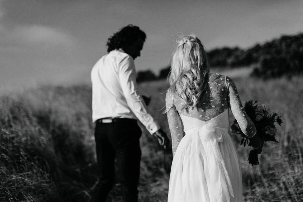 Black and white photo of a romantic couple walking through a grassy field on their wedding day.