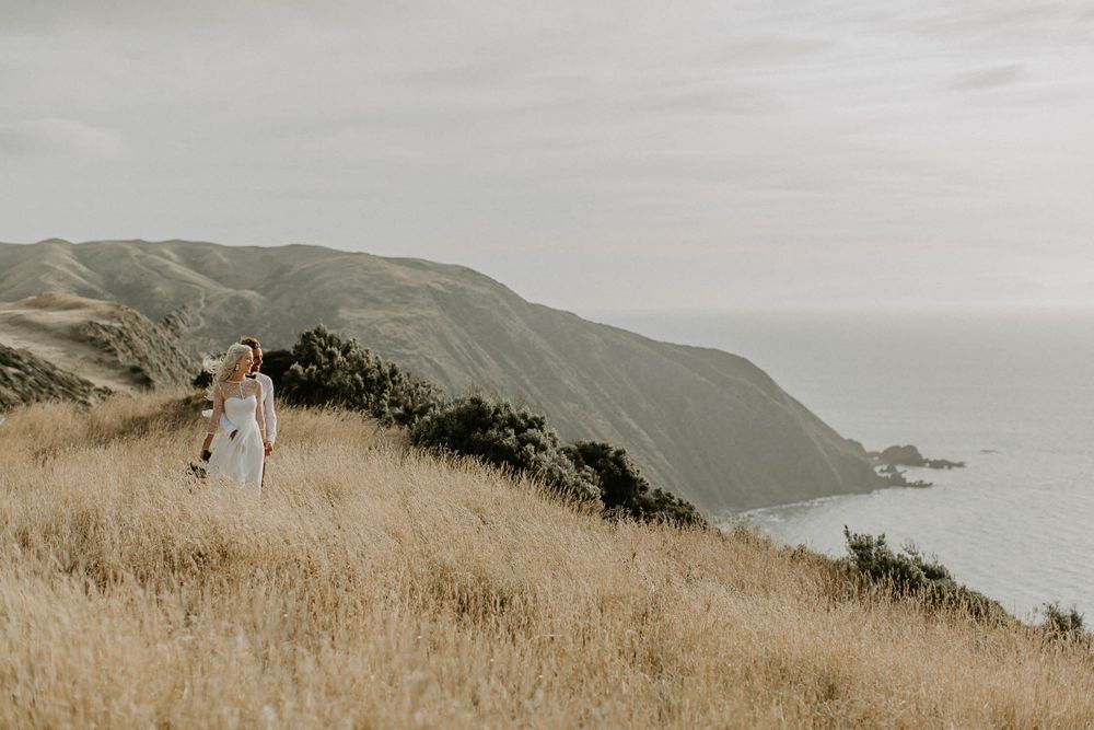 Wedding photo along dramatic coastal cliffs with golden grass and ocean views.