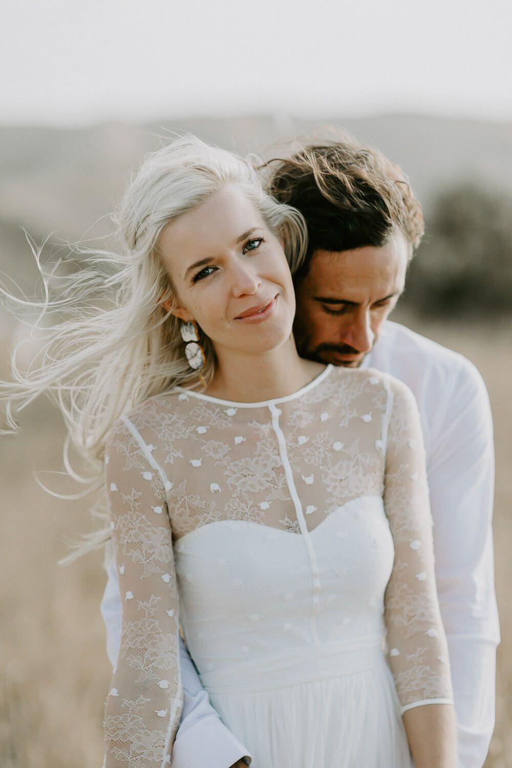 Intimate wedding portrait in a windswept field with soft natural lighting.