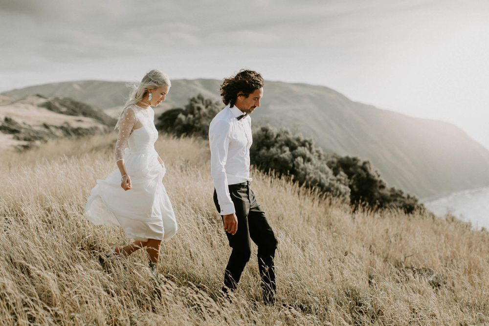 Couple walking through mountain terrain in wedding attire.