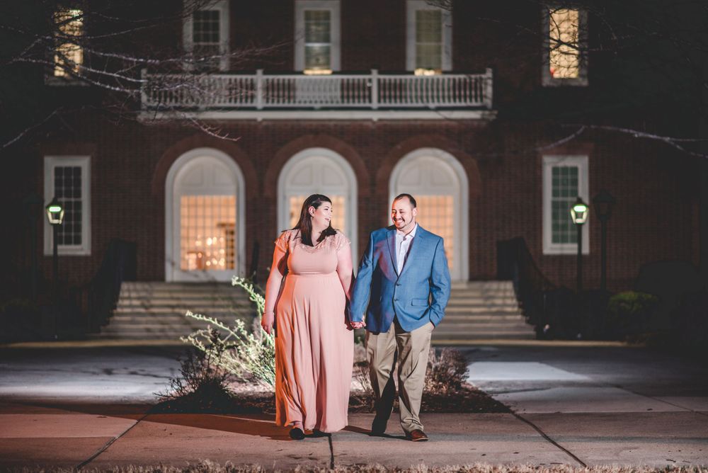 Engagement photo of a couple walking in front of a brick courthouse building at night