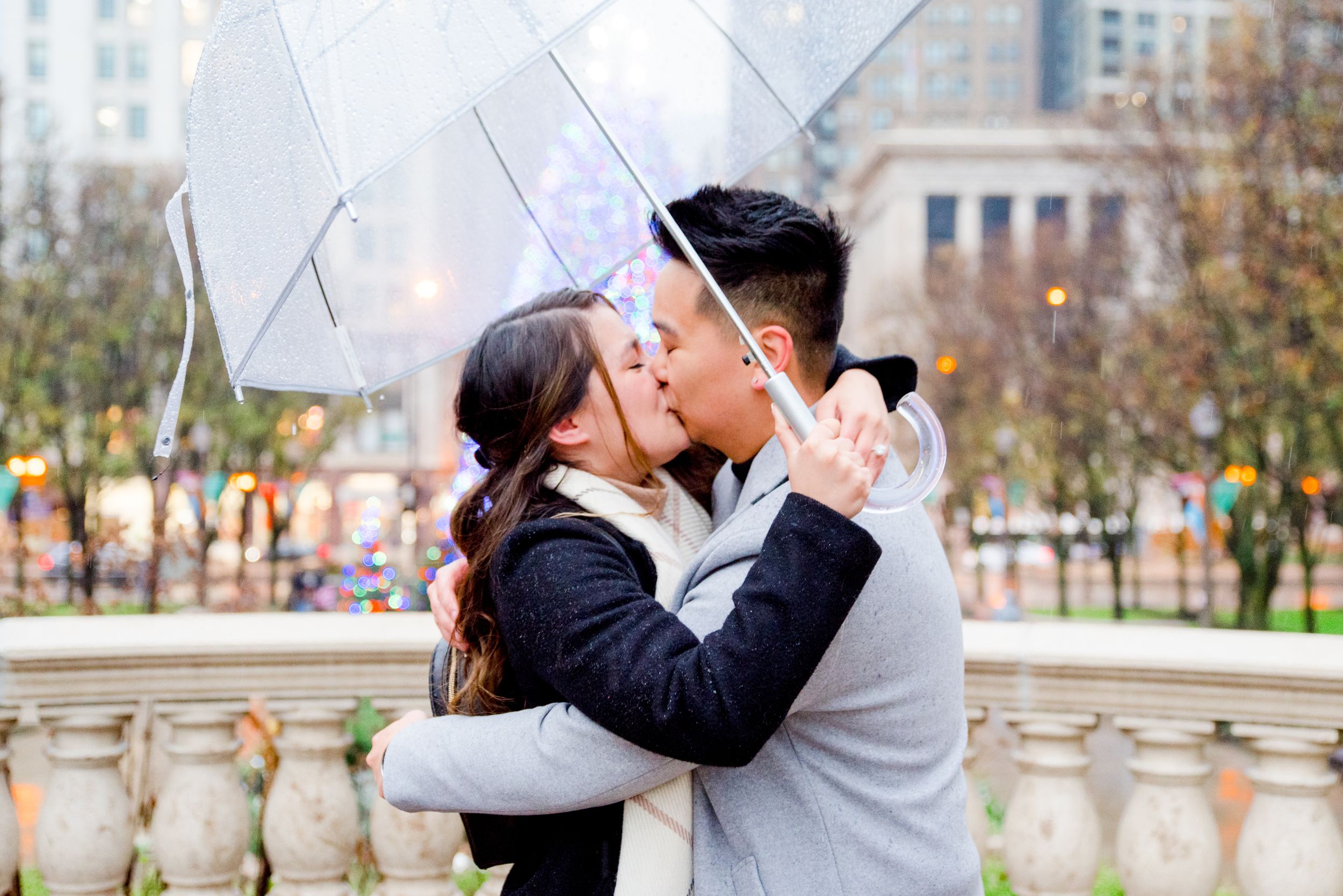 couple hugging under clear umbrella in front of Millennium Park Christmas Tree