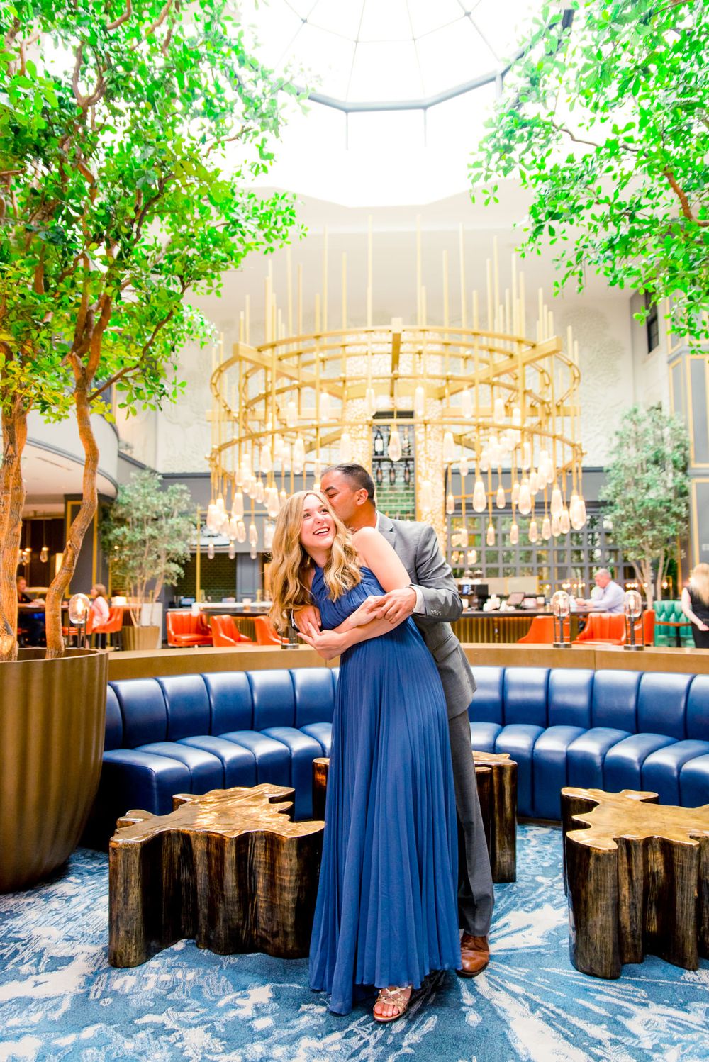 man in grey suit hugs woman in blue dress from behind in front of gold chandelier at Lytle Park Hotel bar