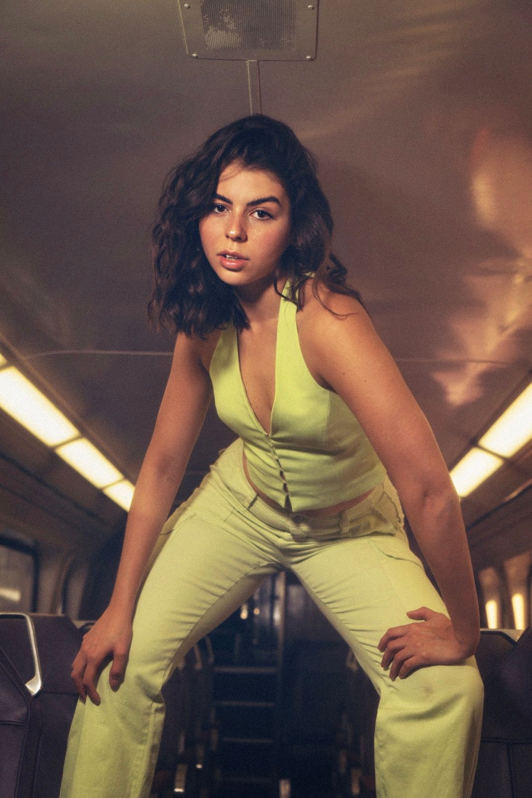 Retro-styled photo of someone in lime green outfit posing dramatically on public transit.
