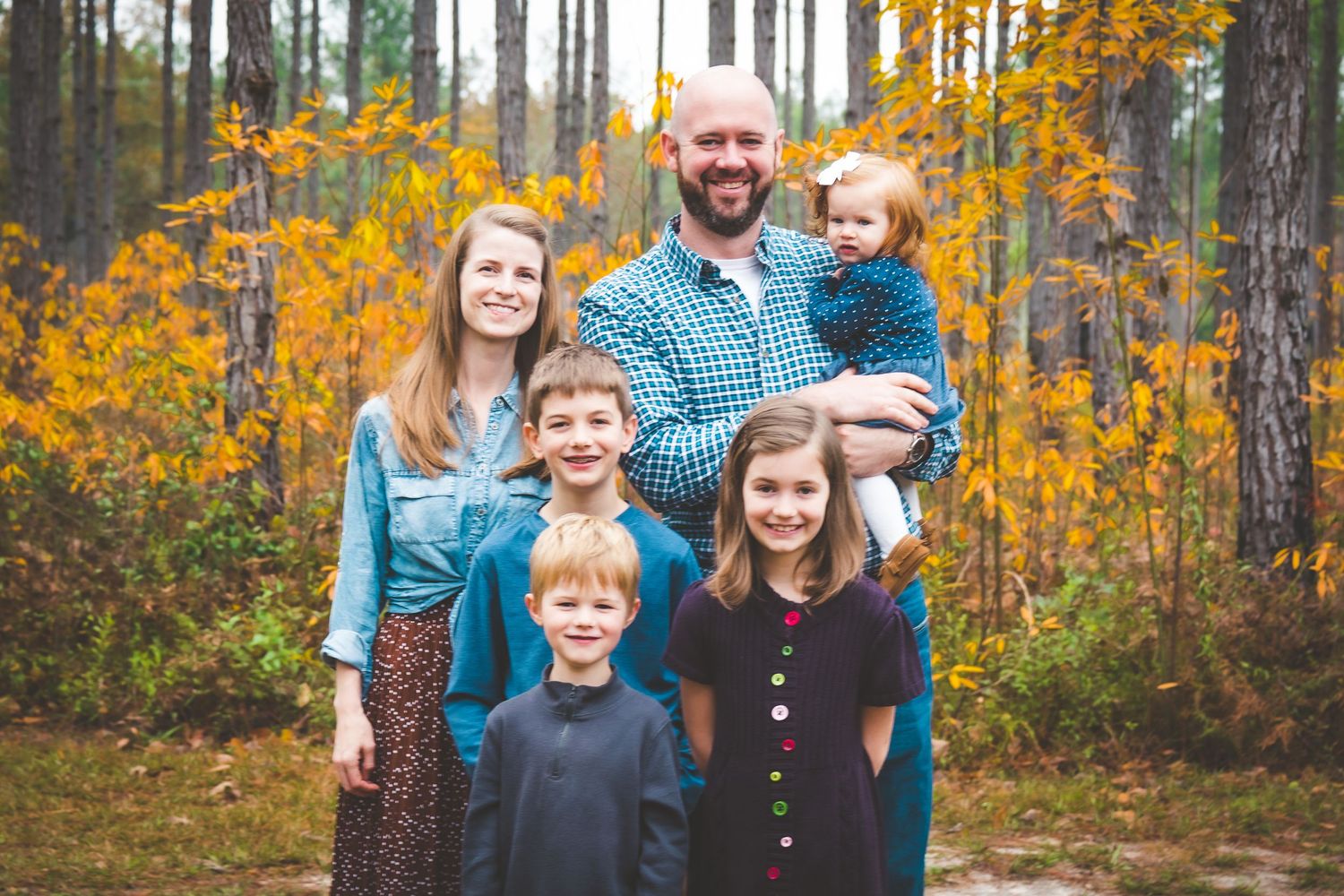 A group poses for a photo in a forest during autumn with yellow foliage in the background.