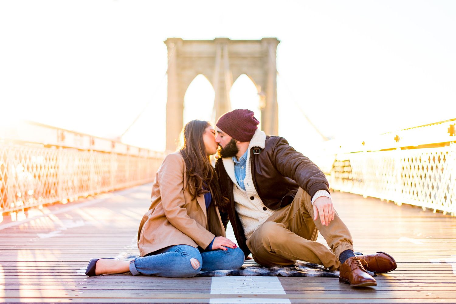 engaged couple sitting and kissing in the middle of Brooklyn Bridge at sunrise in November