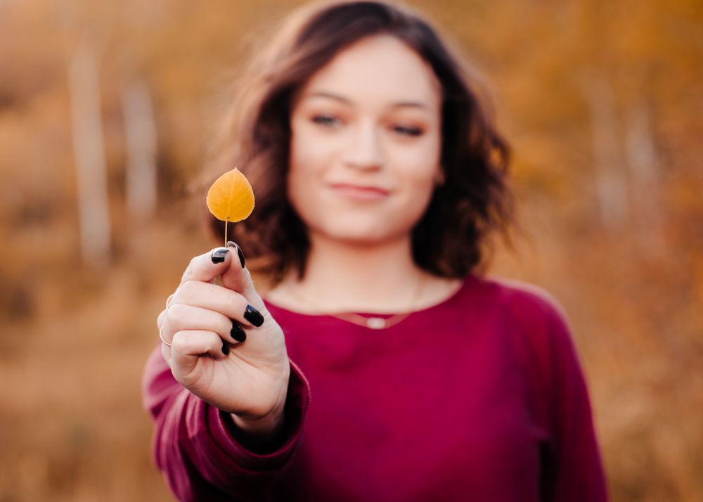 senior girl holding an aspen leaf in her hand