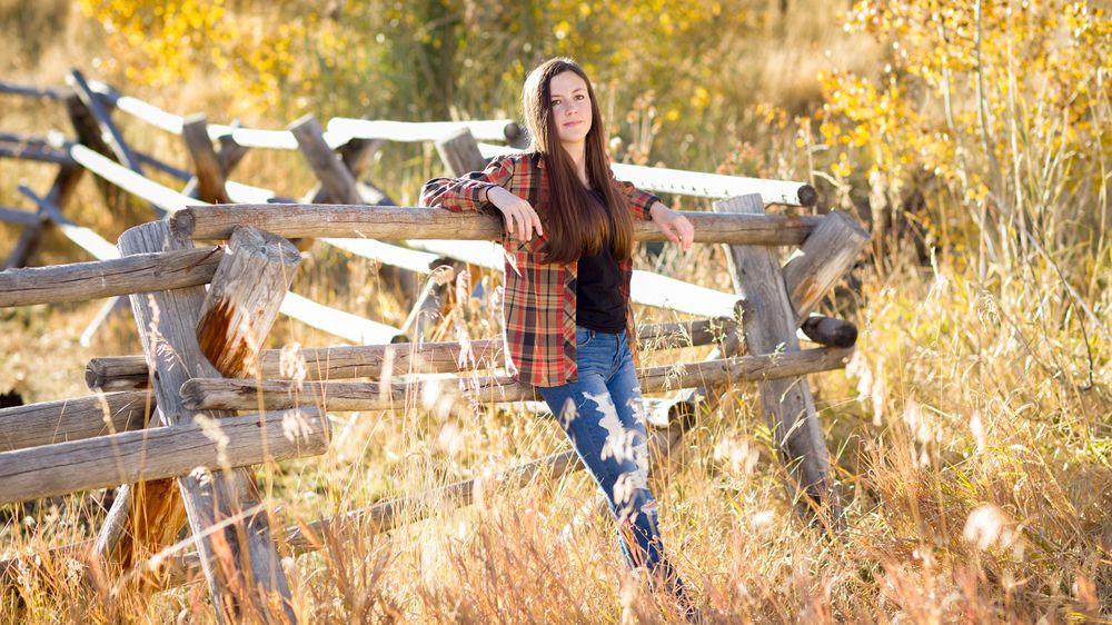 Senior girl standing against a rustic fence