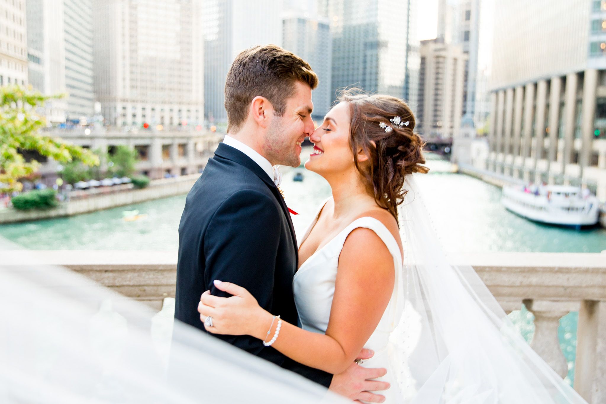 bride wearing a jeweled barette caresses her groom on a bridge in downtown chicago