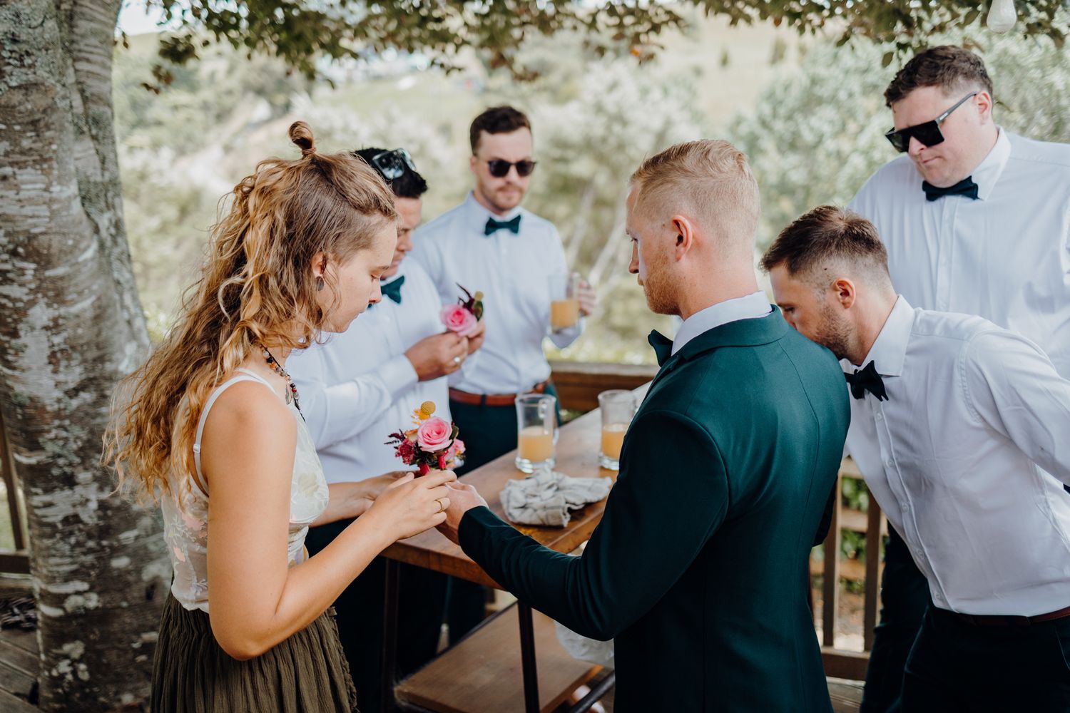 Wedding guests gathered outdoors sharing drinks and conversation under trees.