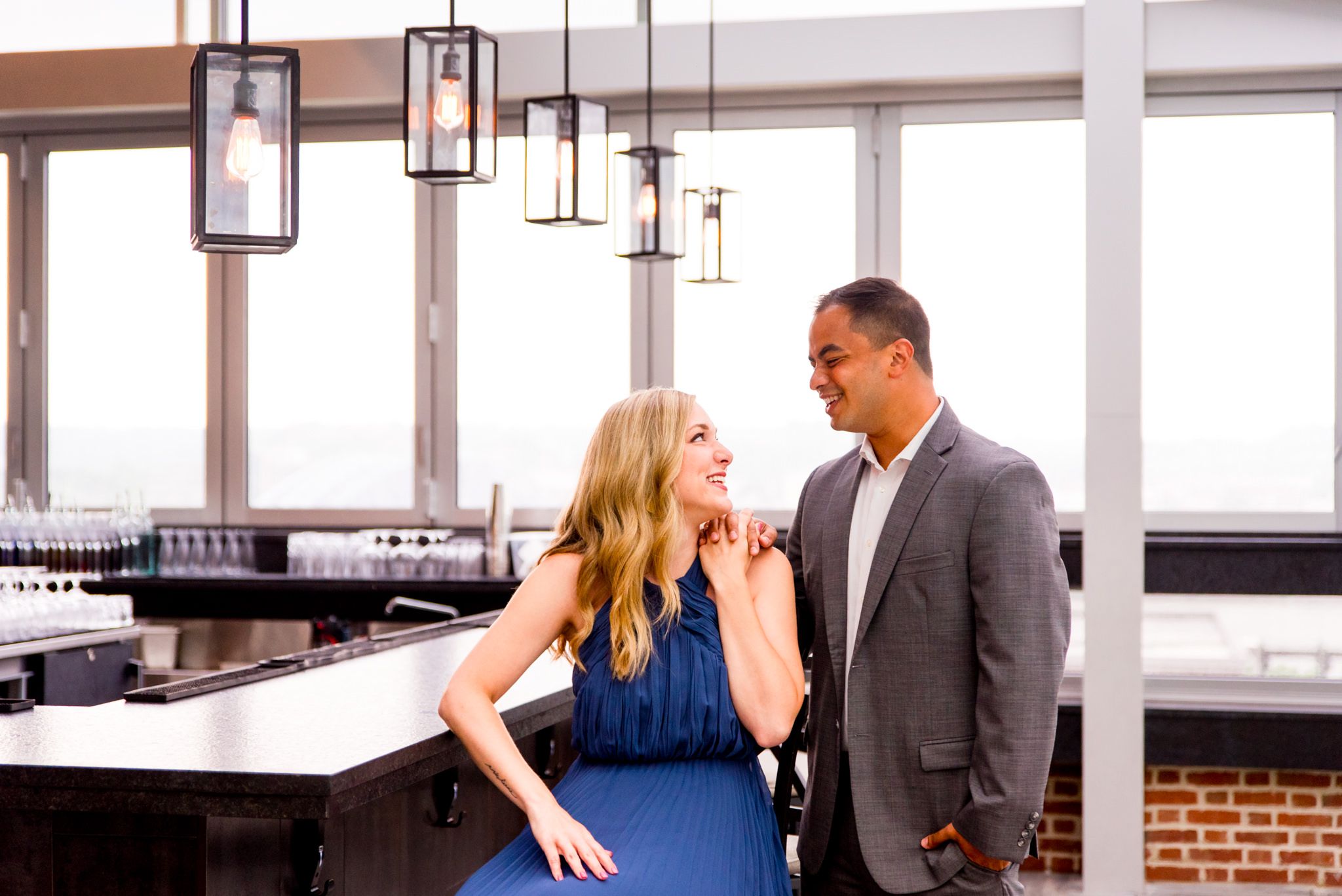 Asian man and blonde white woman hold hands and smile at each other at Vista, rooftop bar at Lytle Park Hotel