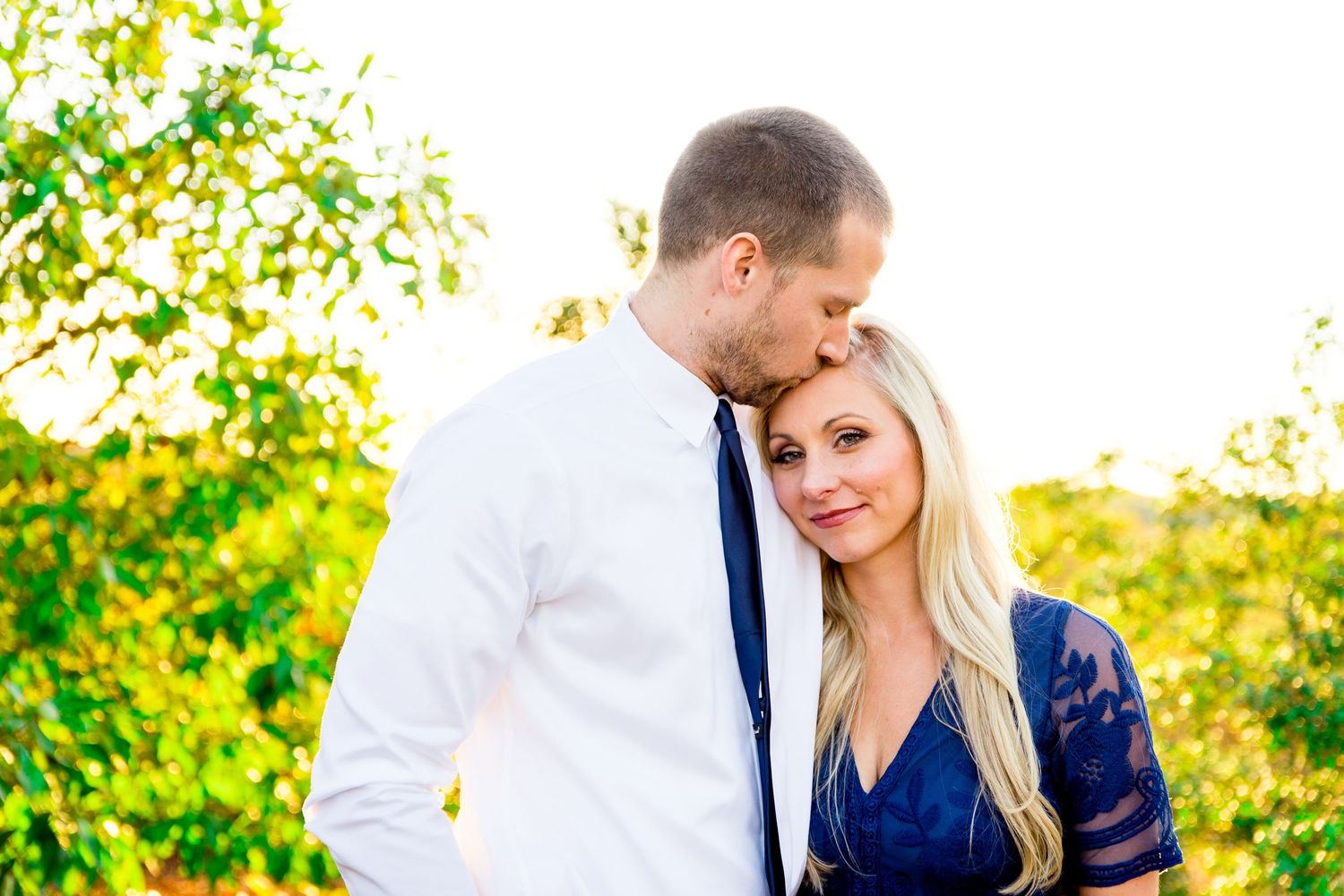 husband kisses blonde wife in navy lace dress on the forehead at sunset in Grant Park Chicago