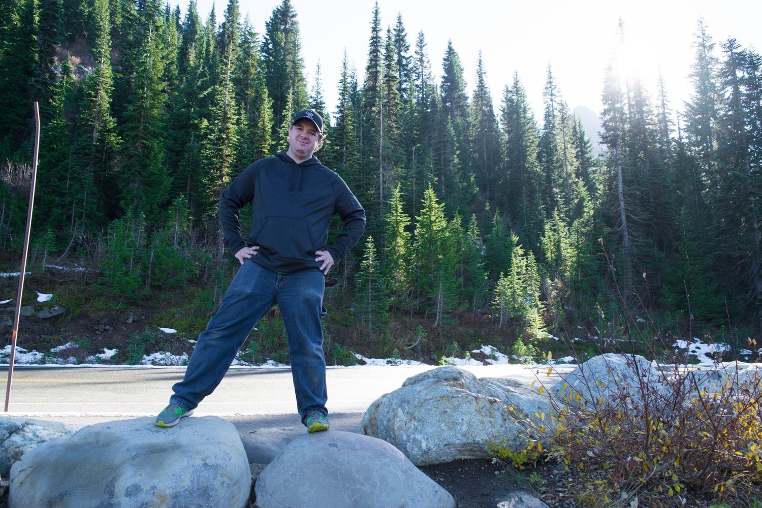 Person stands triumphantly on large rocks with evergreen forest backdrop.