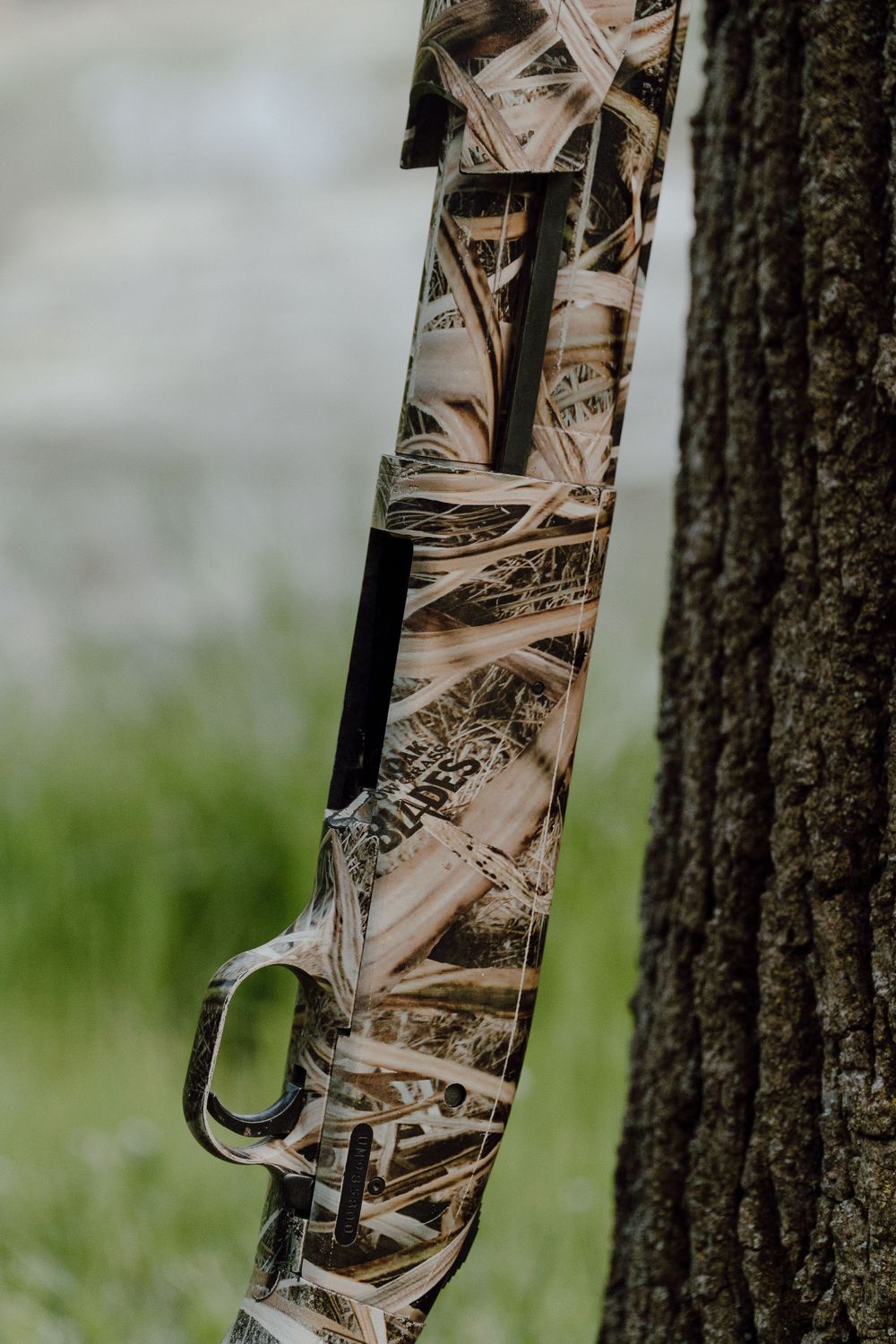 Close-up of a camouflage patterned hunting rifle leaning against a tree trunk.