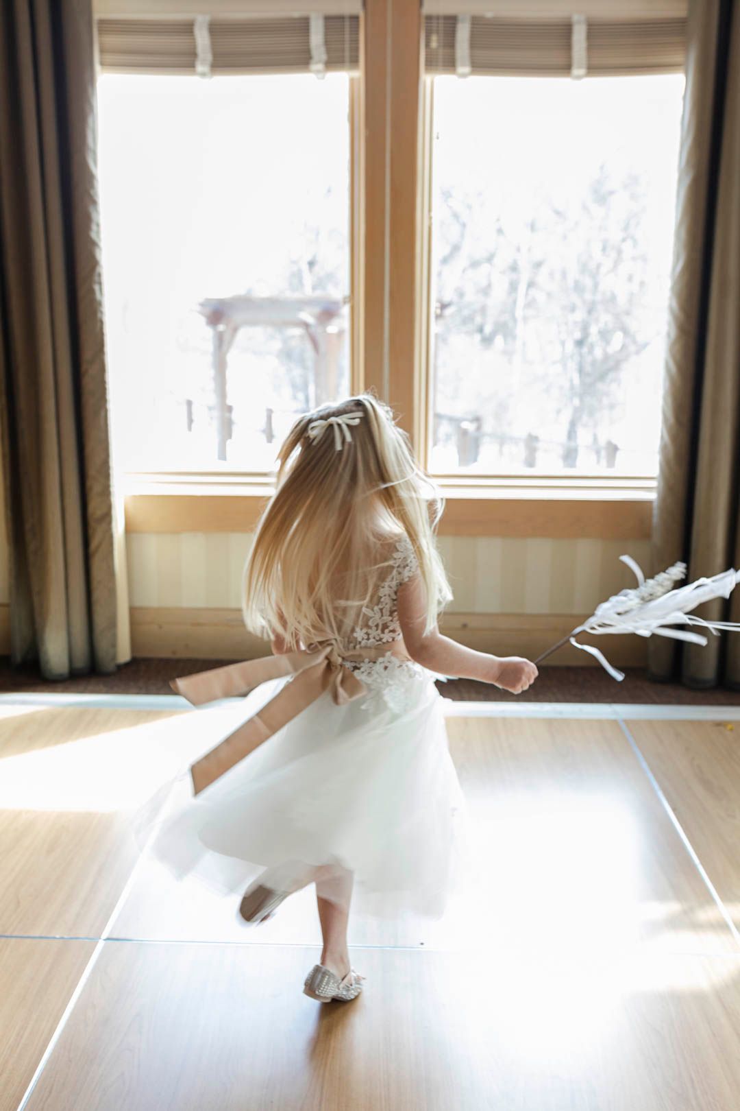 Snowy Wedding In minnesota Flower Girl Twirls inside with wand and snow peeks through the window