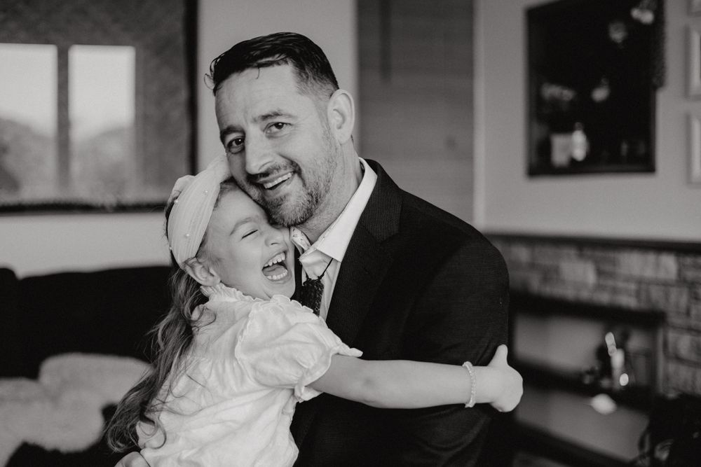 Black and white photo of tender moment between adult and child hugging in living room setting.
